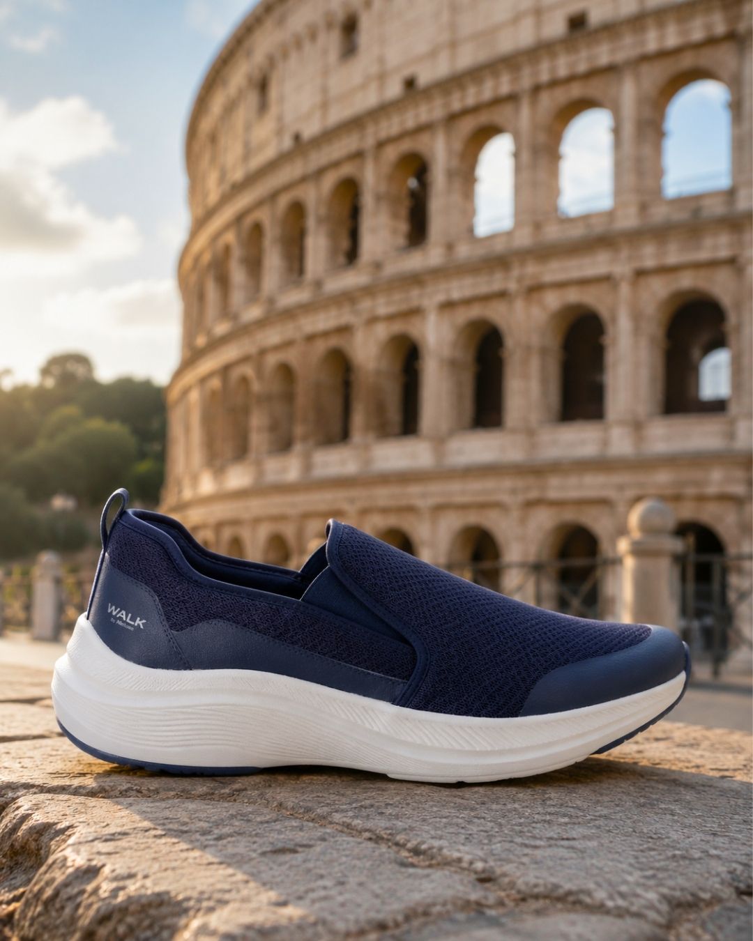 Navy slip-on walking shoe on stone ledge with the Colosseum in Rome at golden hour — comfortable travel sneaker for tours