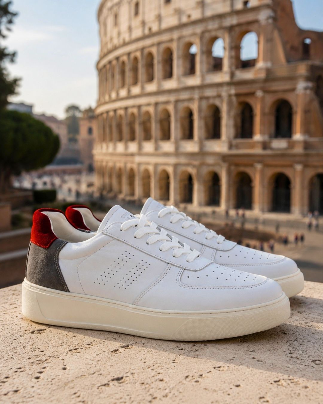 White leather sneakers with red heel detail on a stone ledge, Colosseum in Rome blurred in the background