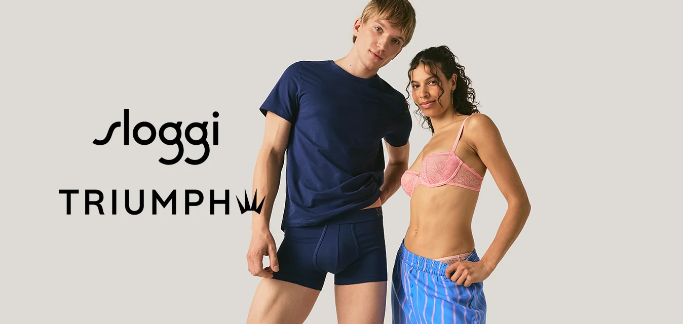Un uomo con una maglietta blu navy e boxer sta accanto a una donna con un reggiseno rosa e pantaloncini blu a righe su uno sfondo semplice.