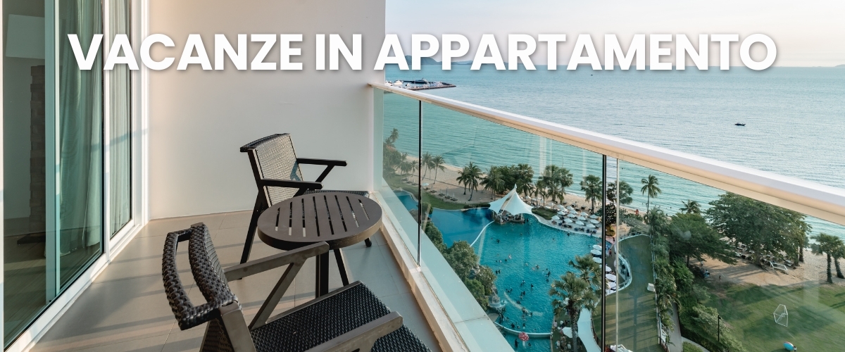 Balcony of beachfront apartment with two wicker chairs and table overlooking resort pool, palm trees and turquoise sea