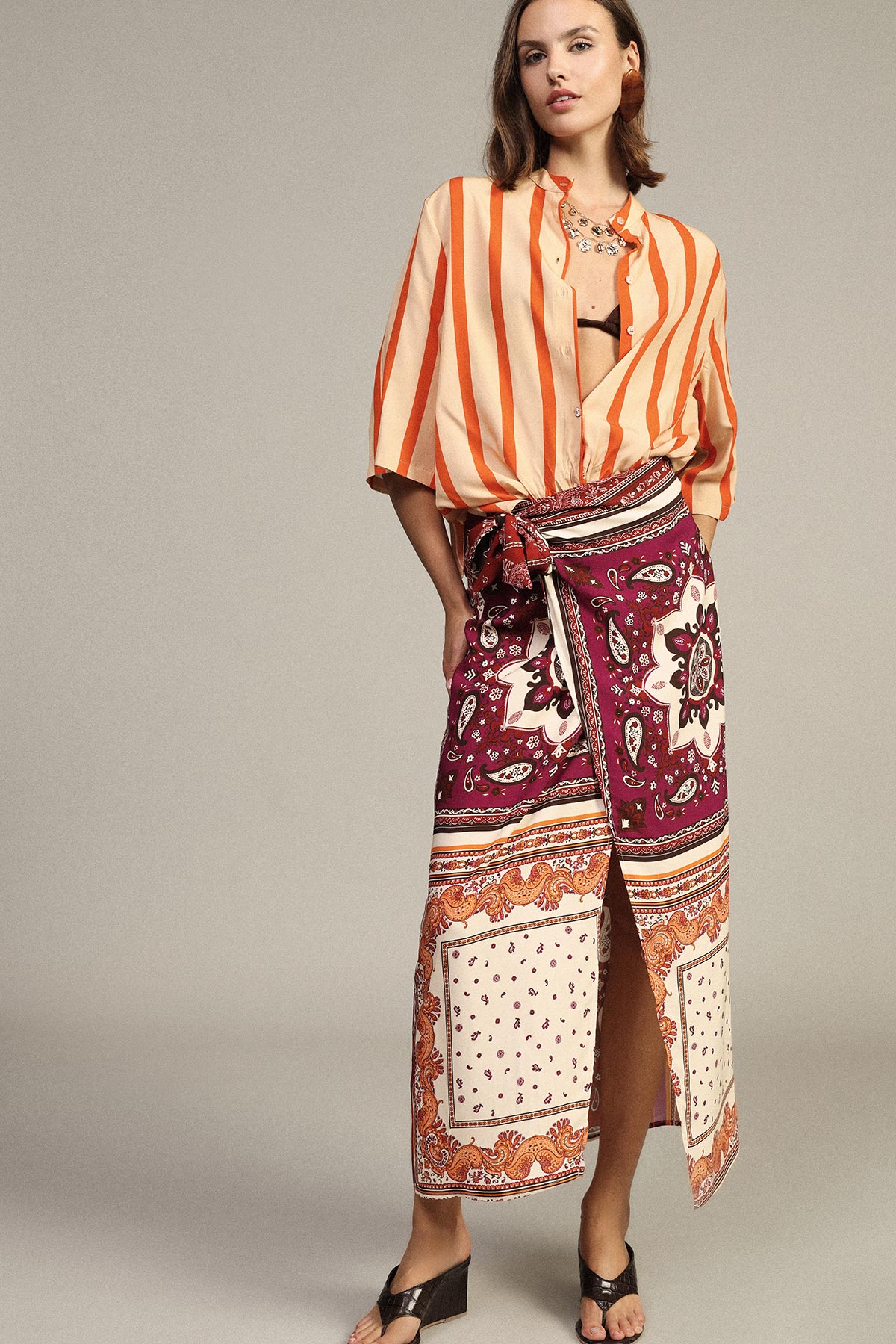 Woman modelling orange striped blouse and patterned burgundy wrap skirt with side slit and black sandals