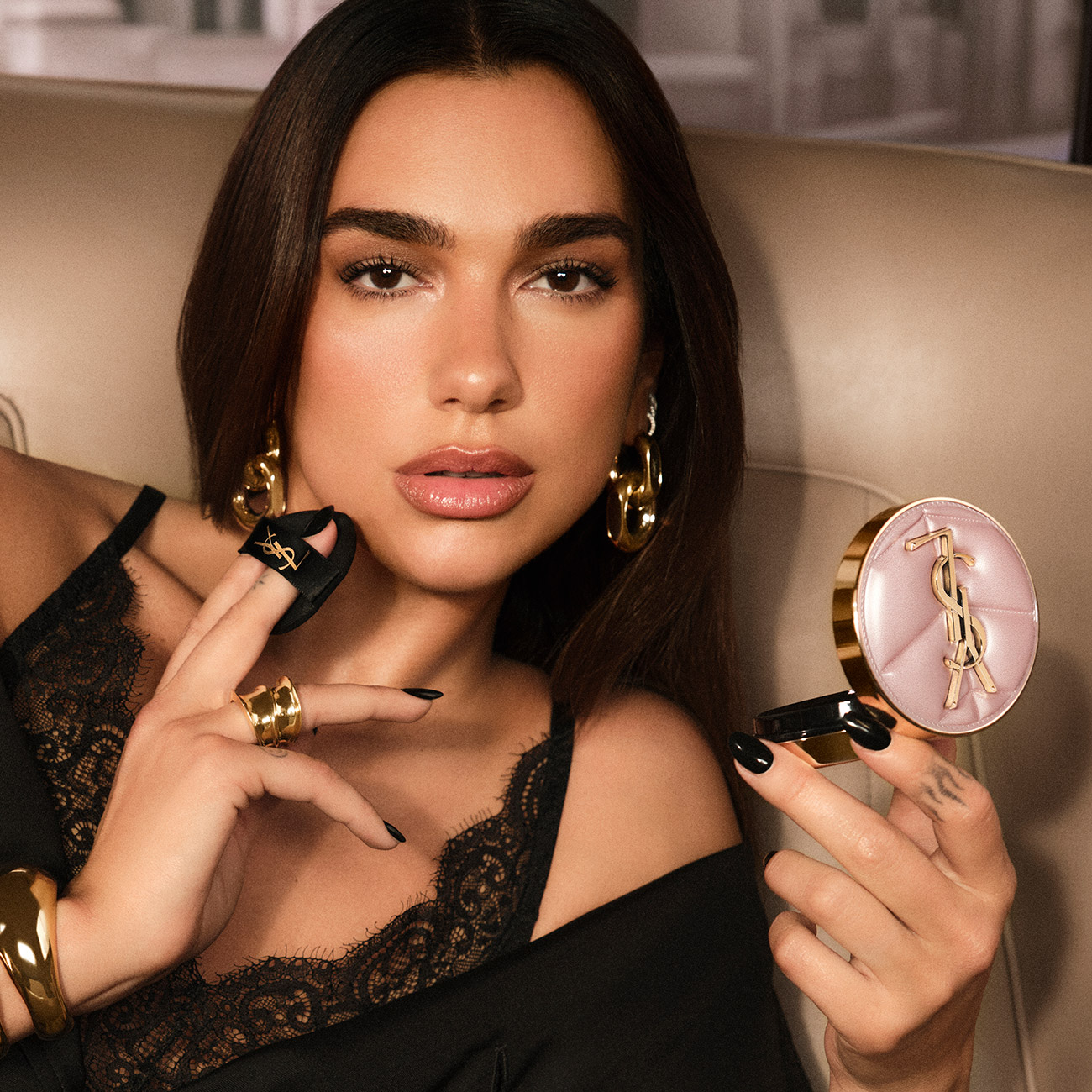 La cantante Dua Lipa si trucca mentre tiene in mano un fondotinta cushion di lusso YSL con astuccio rosa chiaro trapuntato.