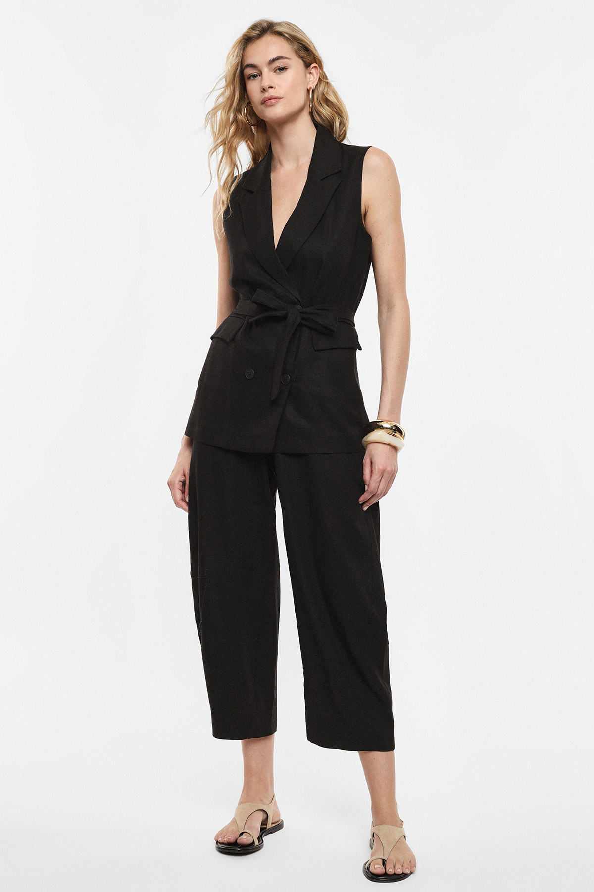 Woman modelling sleeveless black belted blazer vest with matching cropped wide-leg trousers and beige sandals