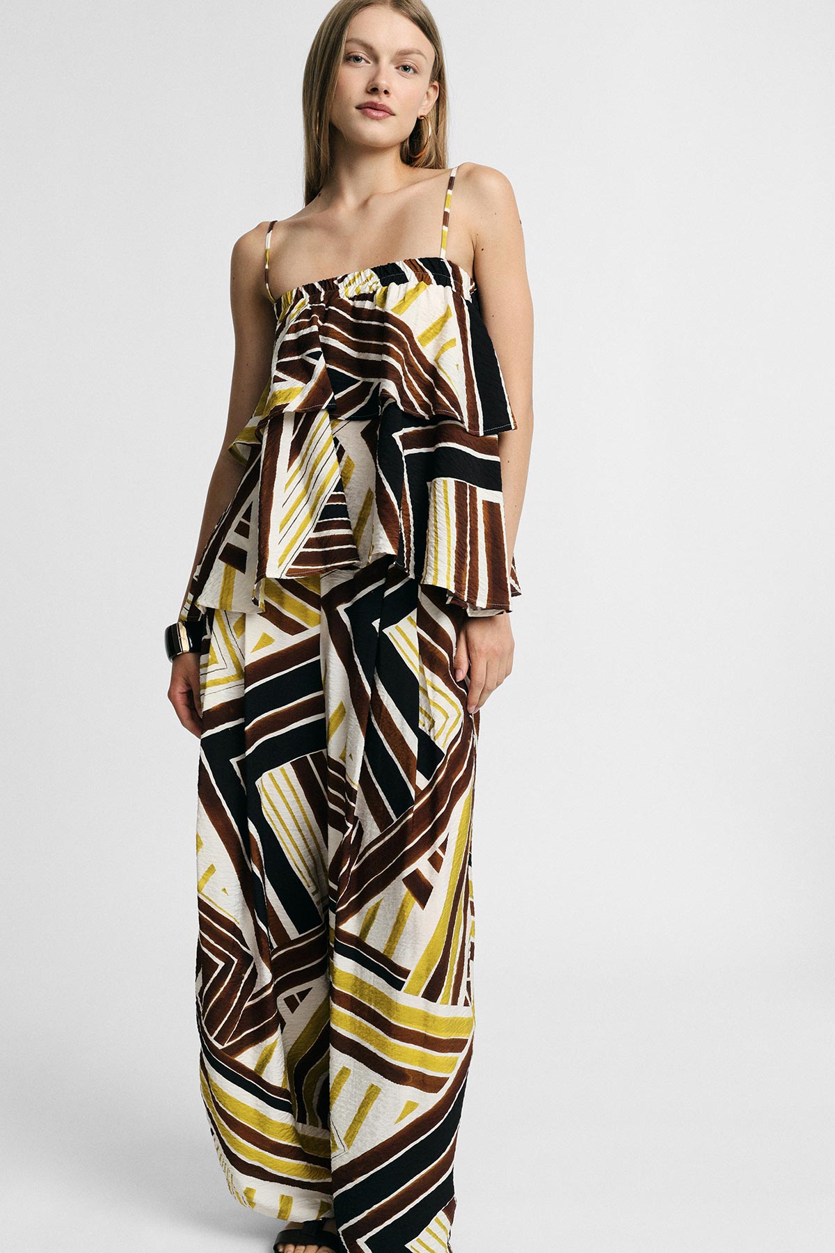 Model wearing matching geometric-print wide-leg trousers and ruffled strapless top in brown, yellow and black