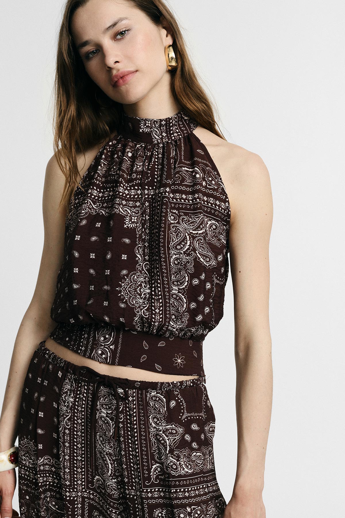 Woman wearing brown bandana-print halter crop top and matching co-ord trousers, gold hoop earring, casual summer outfit
