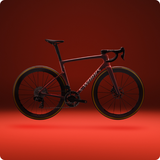 Profile of a red S-Works carbon road bike with deep-section wheels and drop handlebars on a red studio background