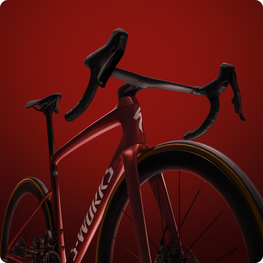 Close-up of a red S-Works aerodynamic road bike with carbon drop handlebars and deep-section wheels on a gradient red background