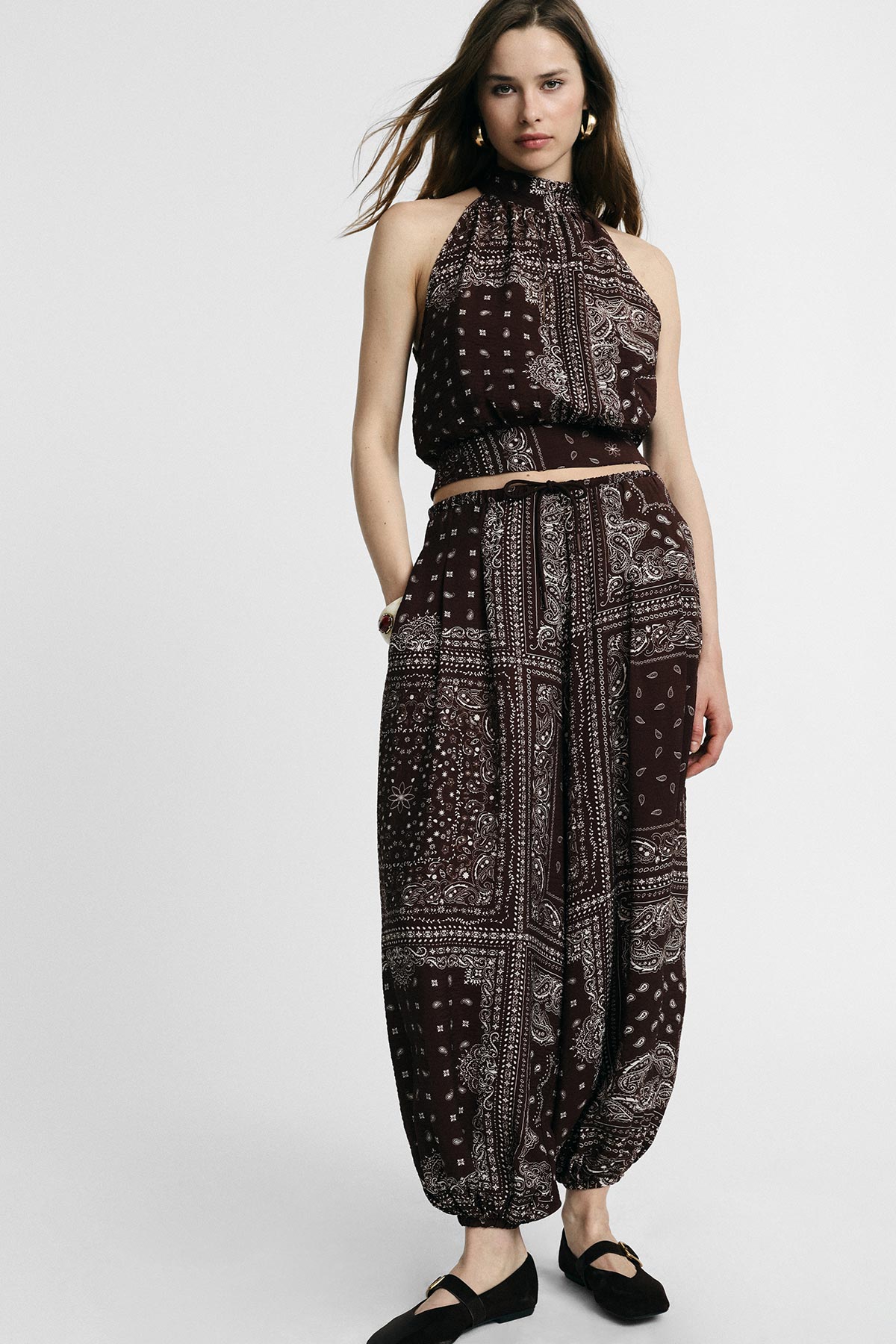 Woman modelling burgundy bandana-print halter crop top and matching high-waist harem trousers with black flats and gold hoops