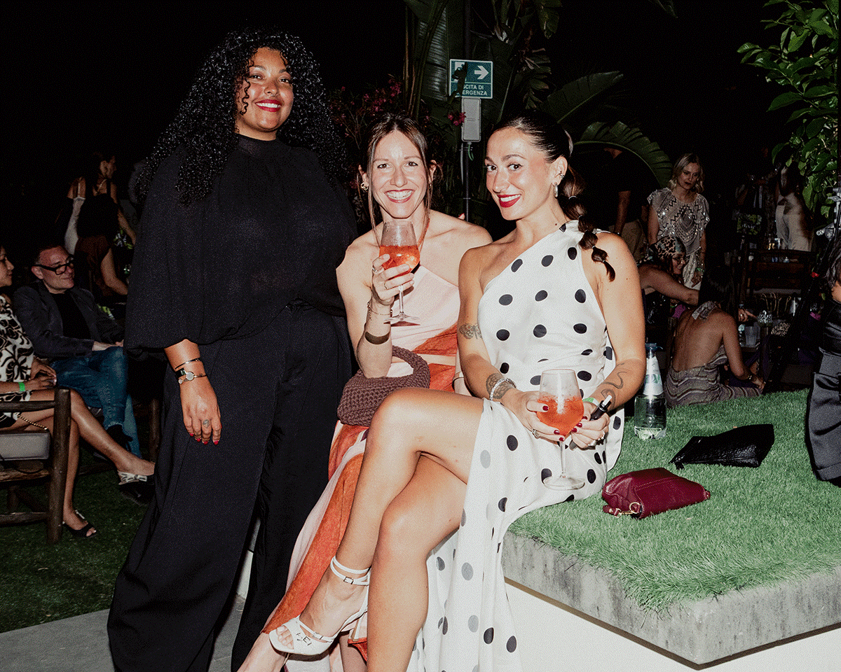 Group of fashionable women smiling and posing with cocktails at an outdoor evening garden party with colourful backdrop