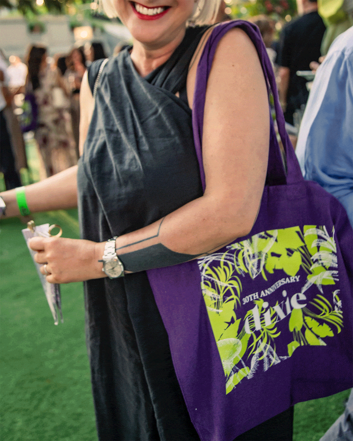Guests mingling at an outdoor summer event with purple branded tote bags and branded snack cones on display