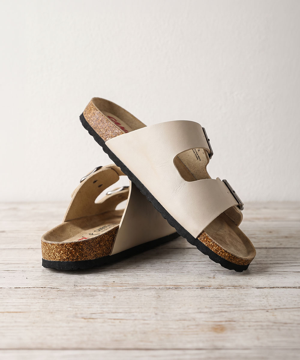 Beige double-strap cork-footbed sandals with adjustable silver buckles on rustic wooden surface