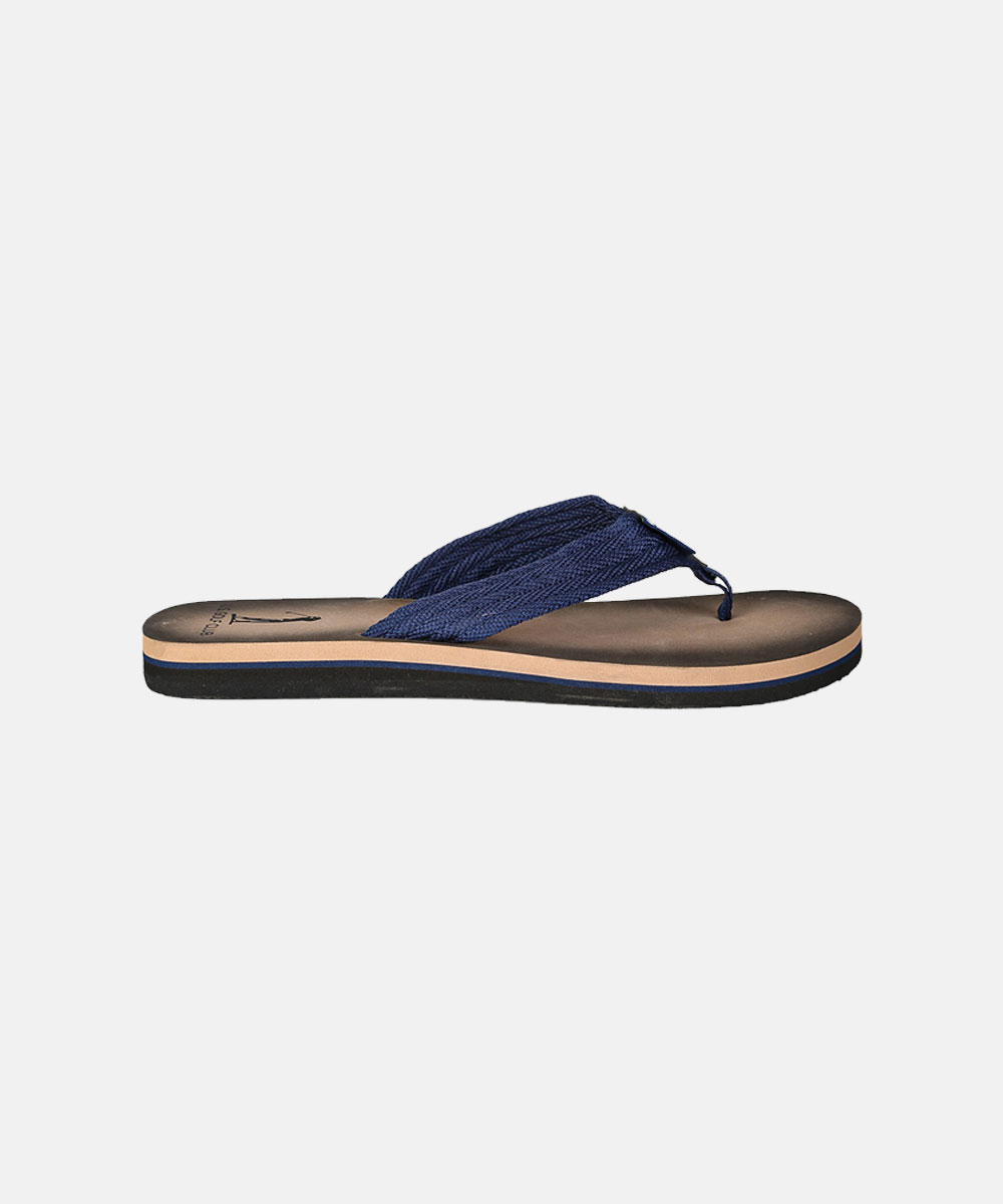 Side view of navy blue fabric-strap flip-flop sandal with tan footbed and layered black sole on white background