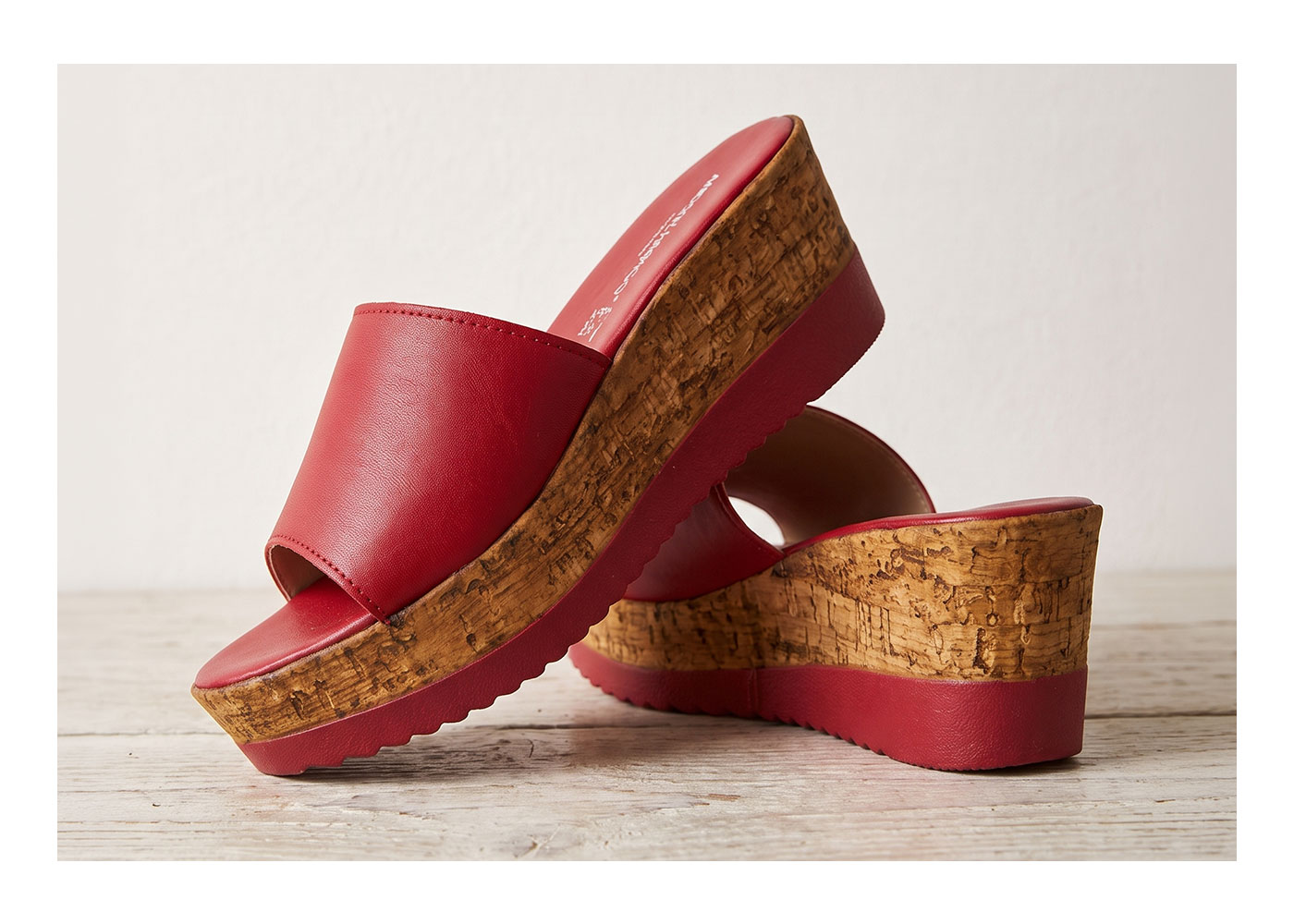 Red leather open-toe wedge sandals with cork platform and textured rubber sole, women's slide heels on wooden surface