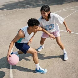 Giovane uomo che palleggia un pallone da basket mentre una giovane donna in maglia bianca lo difende su un campo all’aperto alla luce del giorno.