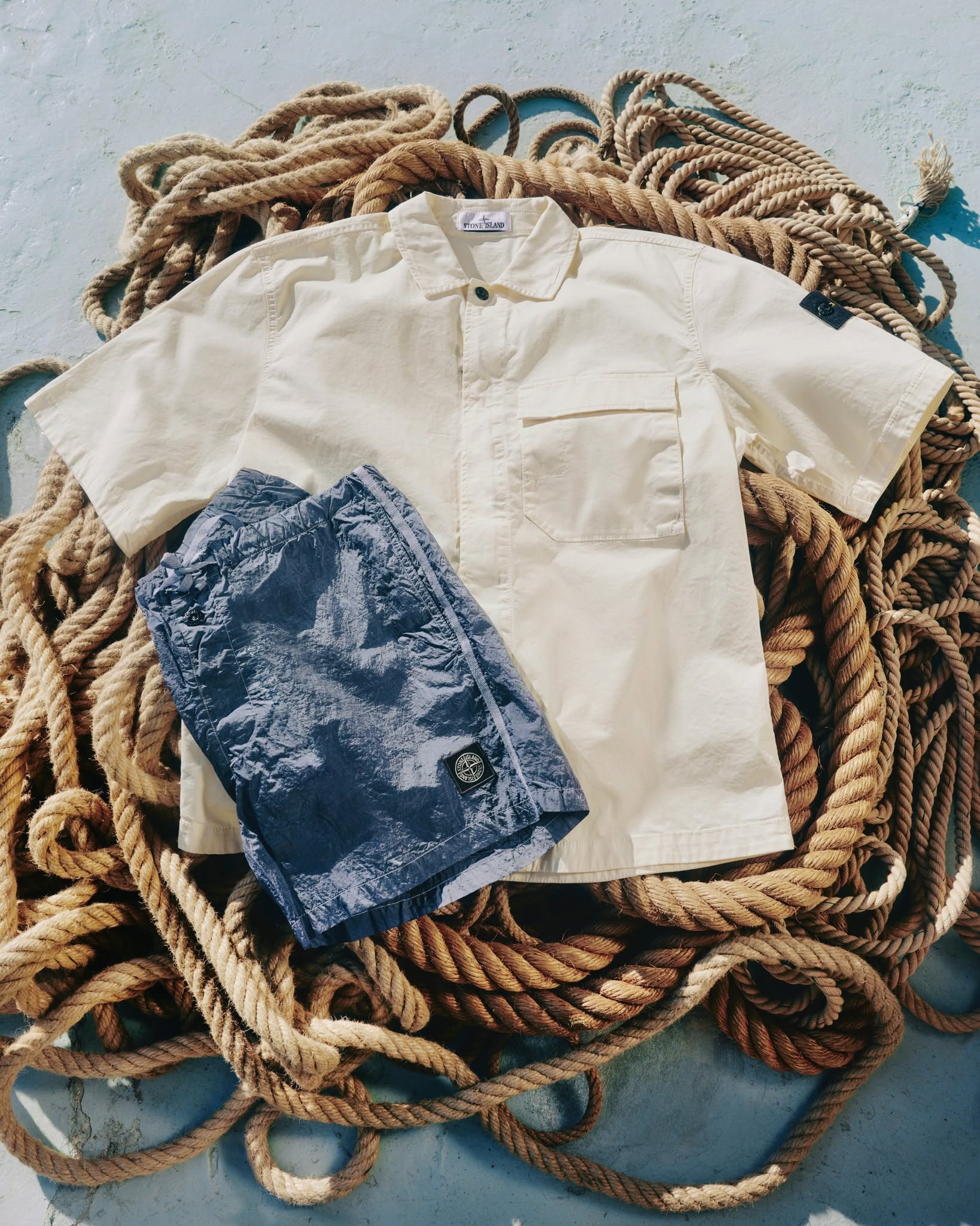 Cream short-sleeve collared shirt and navy crinkled shorts displayed on coiled nautical ropes on deck