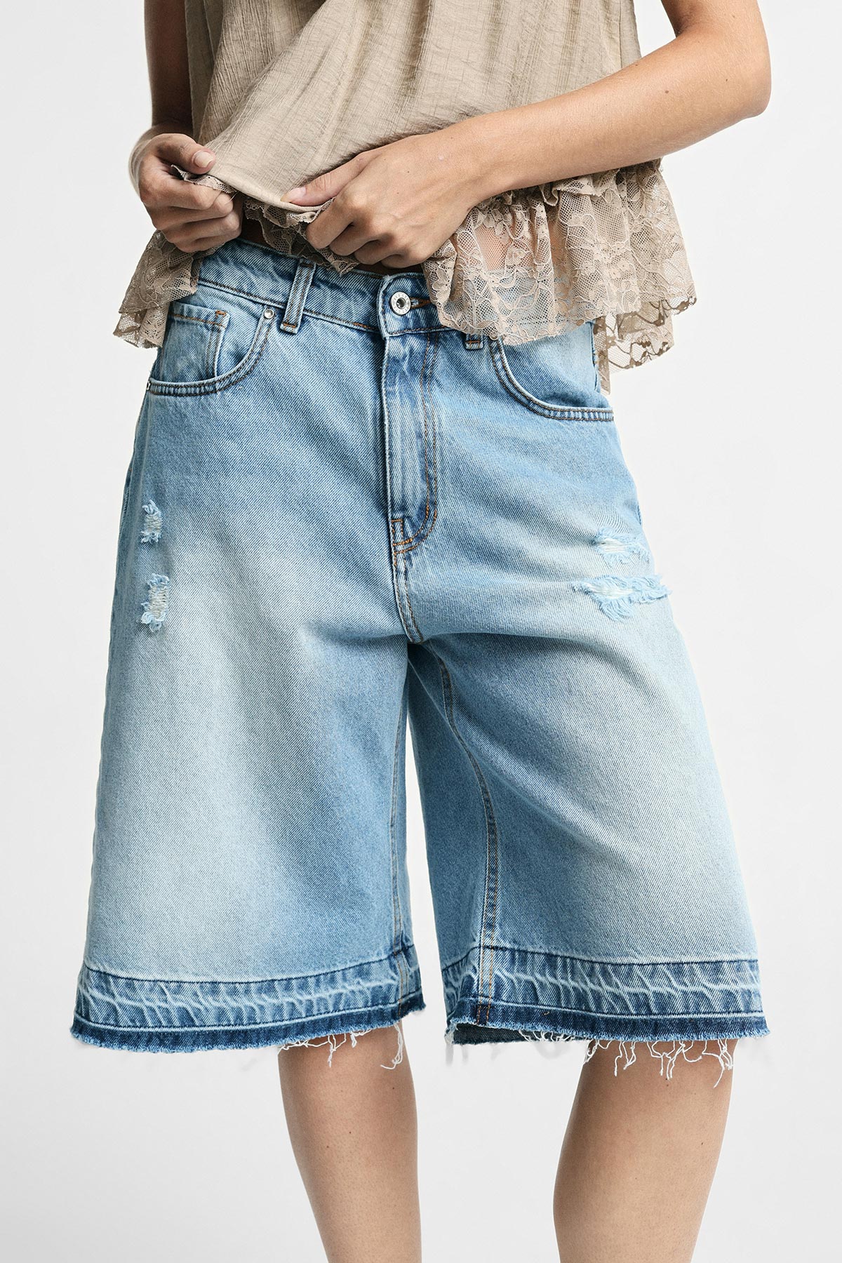 Woman modelling light blue distressed knee-length denim bermuda shorts with frayed hem and beige lace top