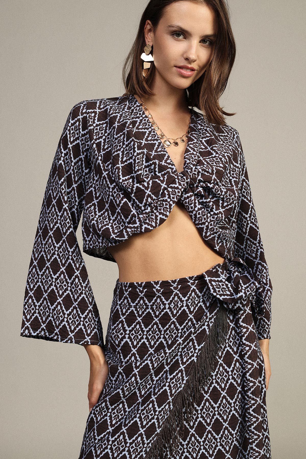 Model wearing navy and pale-blue geometric patterned cropped wrap top with matching high-waist skirt, tie and fringe detail