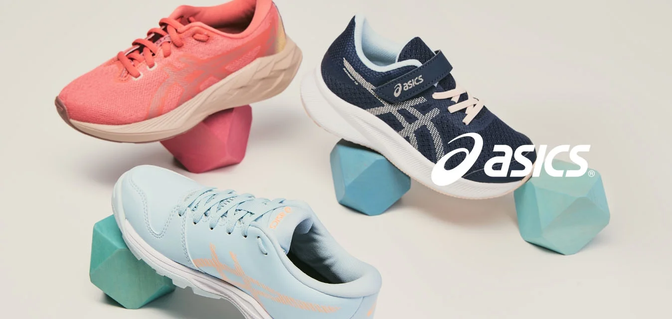 Tre scarpe da ginnastica color corallo, blu navy e azzurro chiaro bilanciate su blocchi di schiuma geometrici su uno sfondo semplice.