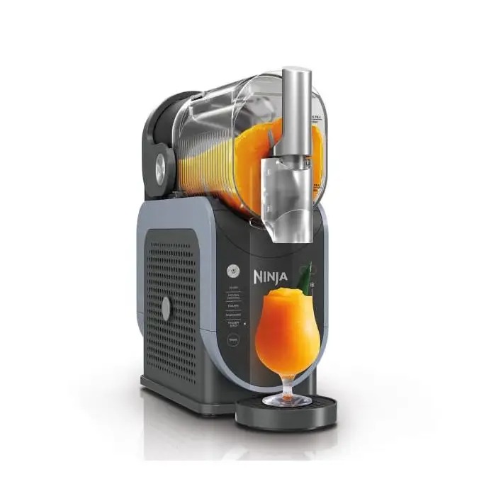 Ninja frozen drink maker on worktop pouring bright orange mango slush into a stemmed cocktail glass