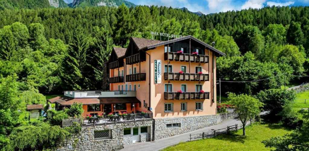 Four-storey Alpine hotel with wooden balconies and flower boxes beside a forested hillside, outdoor terrace and stone base