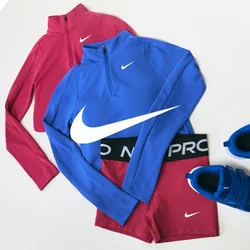 Completo sportivo Nike rosso e blu costituito da due maglie con mezza cerniera, leggings coordinati e un paio di scarpe da ginnastica blu su sfondo bianco.