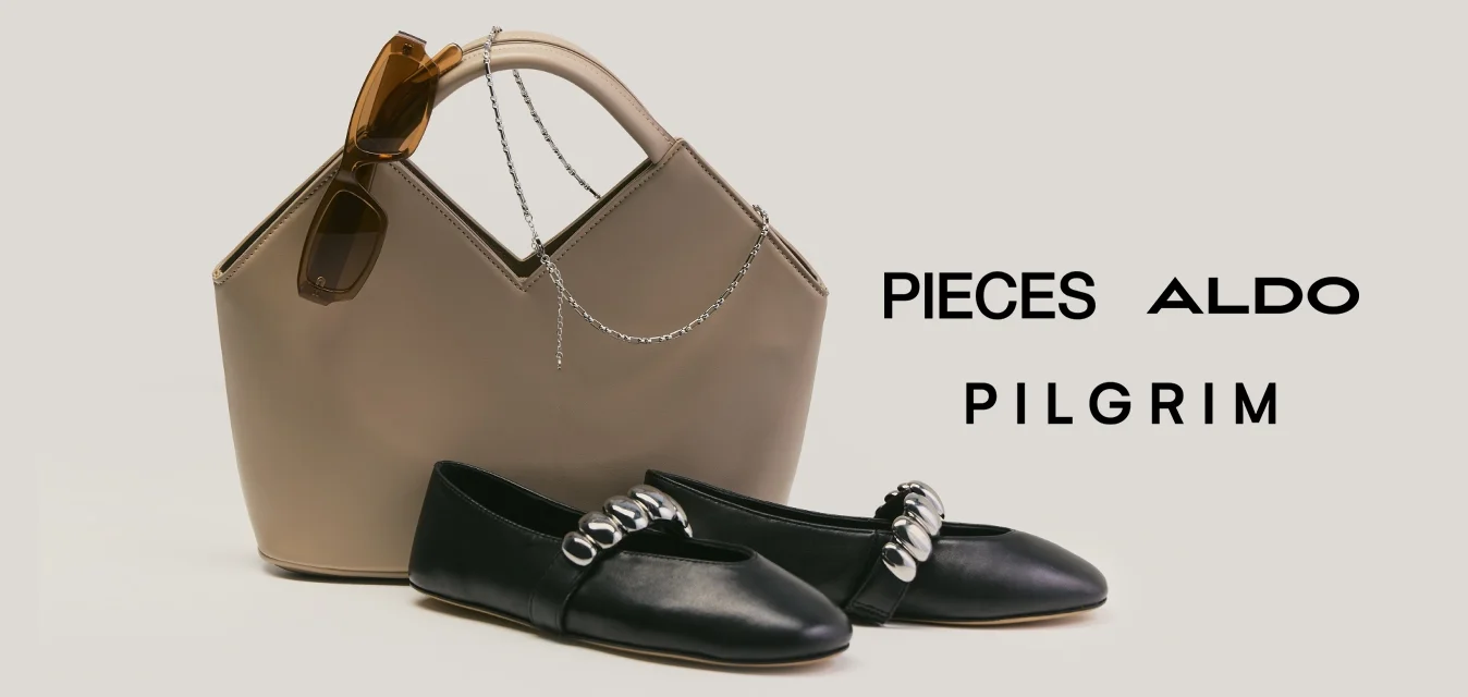 Borsa beige con manici marroni e ciondolo decorativo accanto a ballerine nere in pelle con punta e dettagli di catene d'argento.