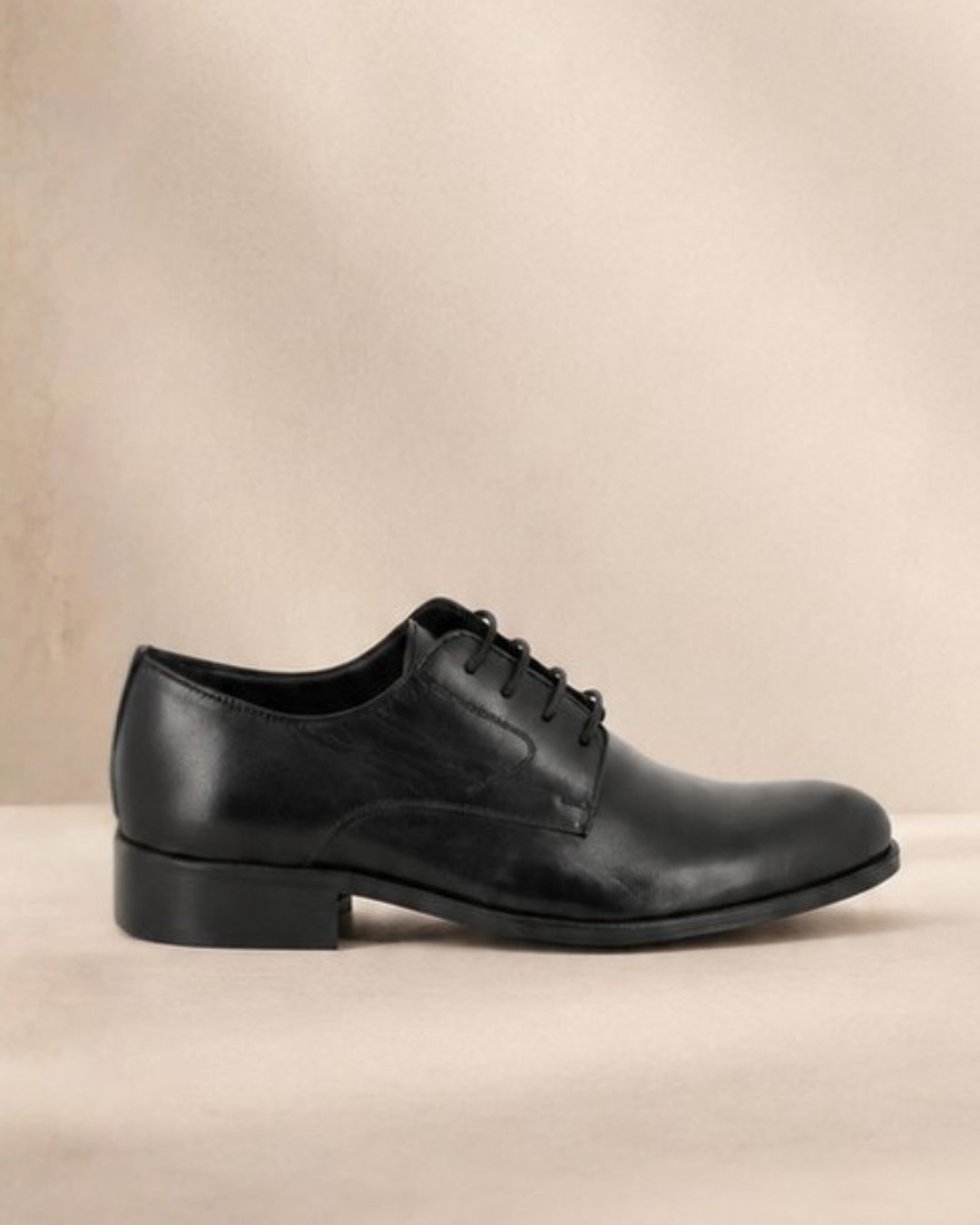 Black leather men's lace-up Oxford dress shoe, side view on a neutral beige background