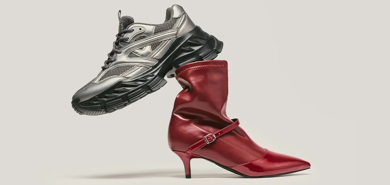 Scarpa da running grigia metallica bilanciata sopra un stivale alto in pelle rossa con cinturino, posizionata su uno sfondo chiaro e semplice.