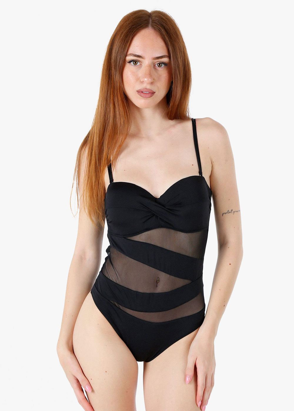 Red-haired woman modelling a black one-piece swimsuit with sheer diagonal mesh panels and thin straps on a white background