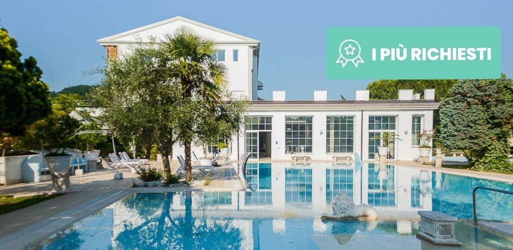 Outdoor hotel swimming pool with sunloungers, palm trees and glass-fronted building reflected in calm water