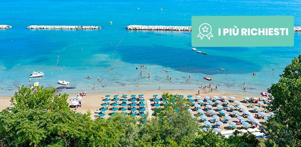 Turquoise Mediterranean beach from hillside, organised rows of sun umbrellas, swimmers, small boats and breakwaters