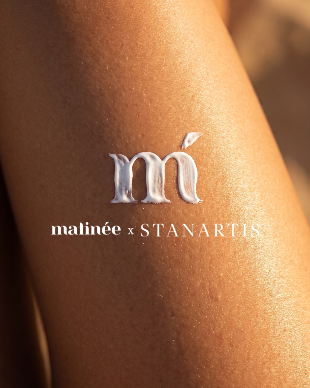 Close-up of sunlit brown leg with white skincare cream shaped into an 'm' above the 'matinée x STANARTIS' logo