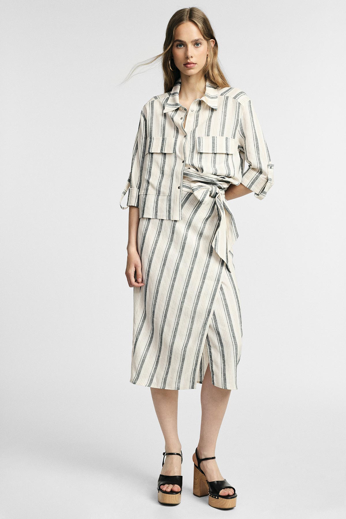 Female model in cream and navy striped button-up jacket with matching wrap midi skirt and black platform sandals