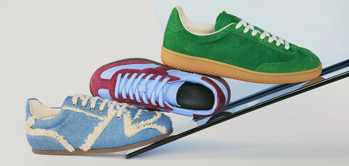 Tre sneaker colorate in blu, rosso e verde bilanciano su una barra metallica nera inclinata su uno sfondo chiaro.