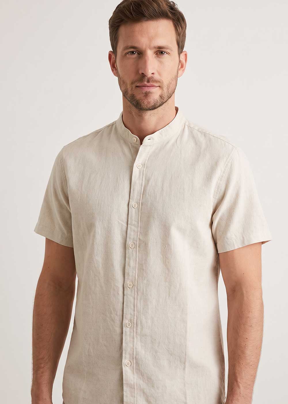 Man wearing beige short-sleeve linen shirt with mandarin collar and front buttons, casual summer men's shirt on neutral background