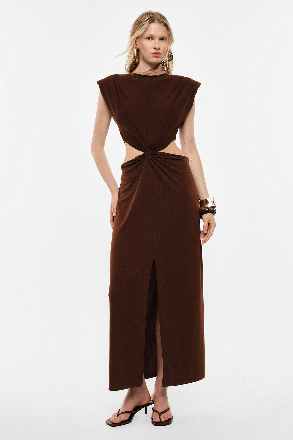 Woman modelling brown cut-out maxi dress with twisted knot and front slit, wearing sandals and bangles