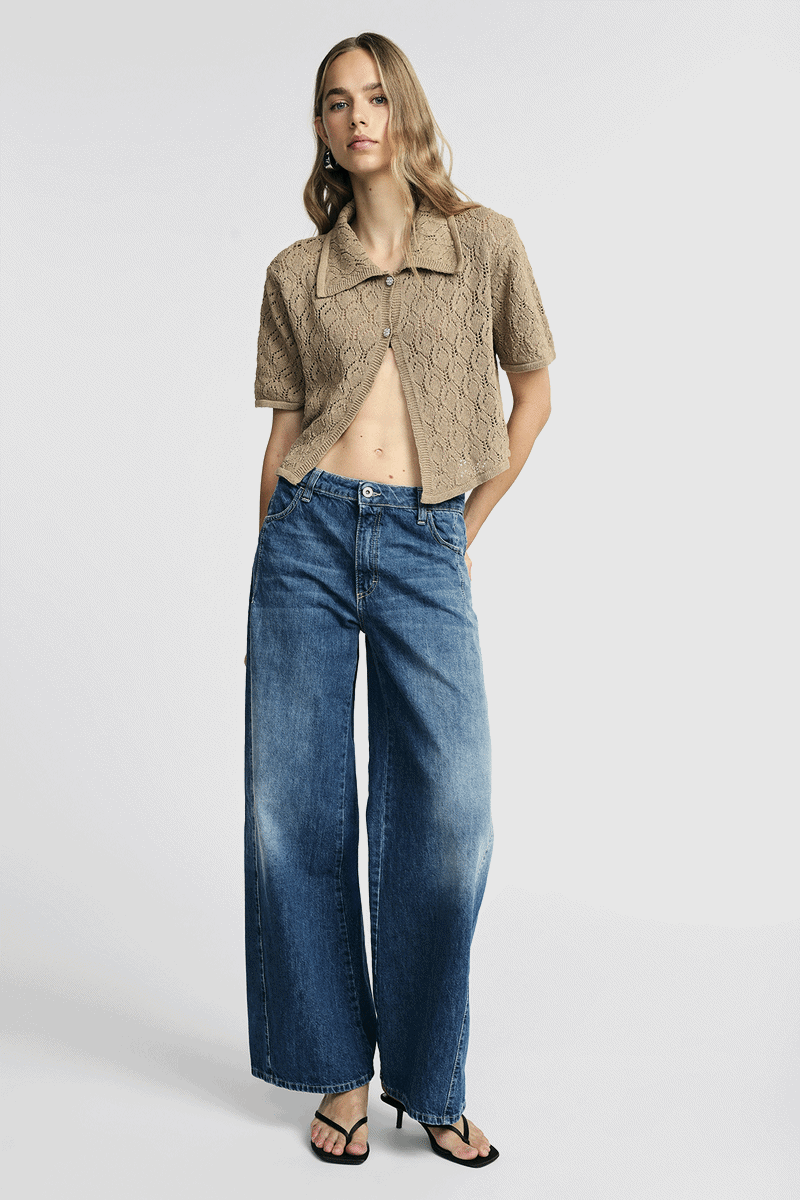 Female model in beige short-sleeve knitted cardigan and high-waisted wide-leg blue jeans with black sandals, studio fashion shot