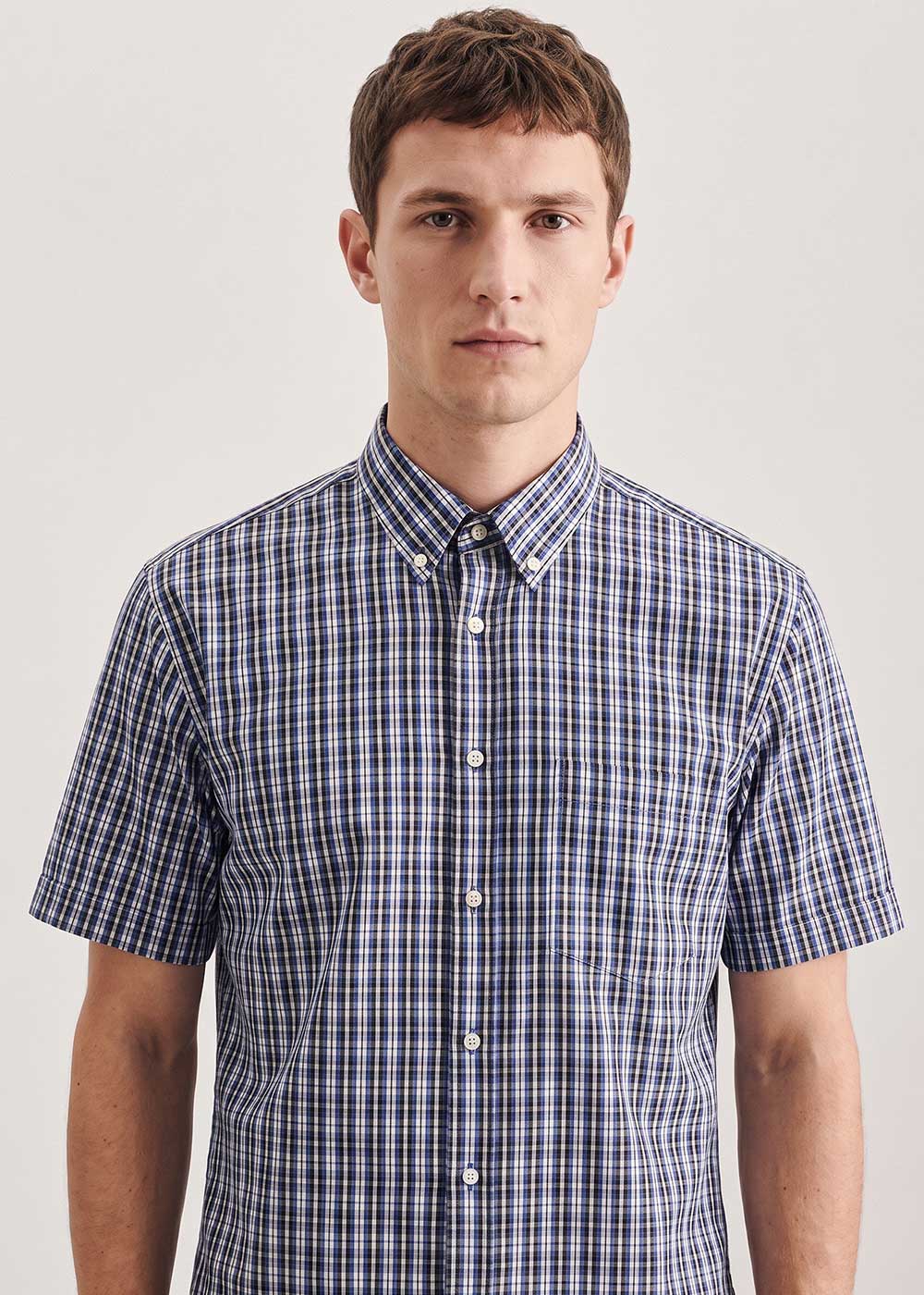 Man wearing navy and white checked short-sleeve button-down shirt, frontal view on a plain light background