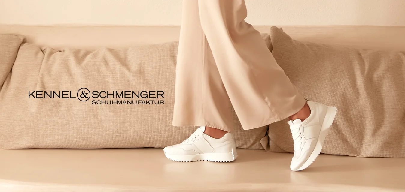 Completo beige con blazer dalla vestibilità ampia e pantaloni a gamba larga, abbinato a sneakers bianche. Ambientato in uno spazio minimalista dai toni neutri.