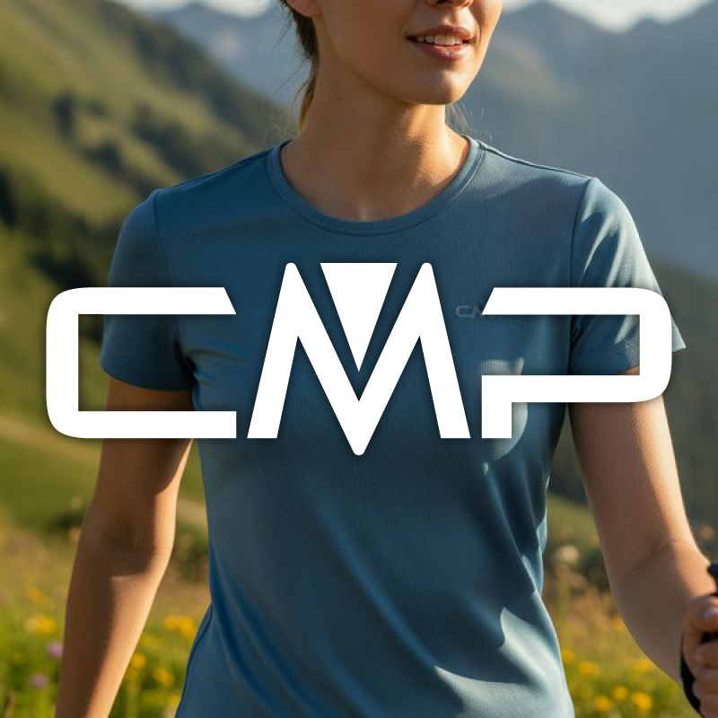 Smiling woman in blue CMP-branded active T-shirt hiking in a sunny alpine meadow with mountains in the background