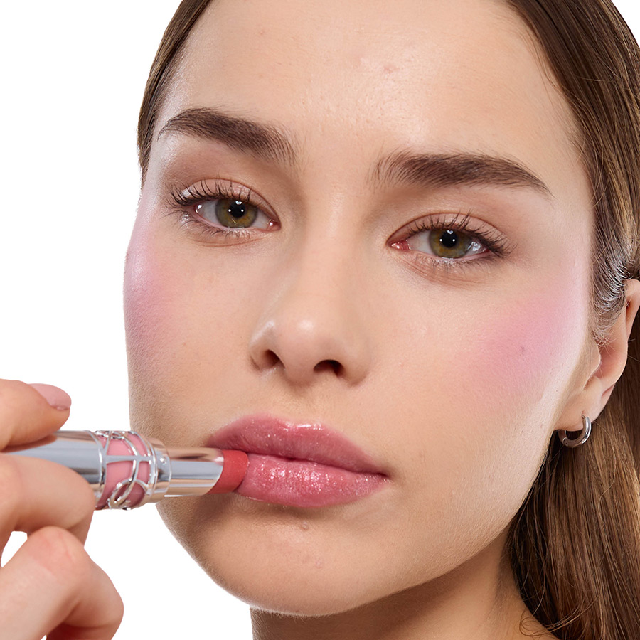 Primo piano di una donna dalla pelle chiara che applica un rossetto rosa brillante YSL sulle labbra.