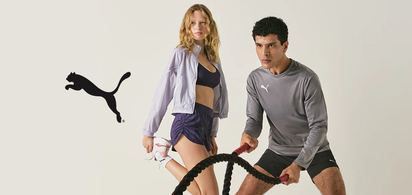 Un uomo usa le battle ropes in una posizione atletica e una donna si allunga la gamba, entrambi indossano abbigliamento sportivo su uno sfondo semplice.
