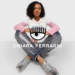T-shirt bianca con maniche a coste rosa, dotata di una grafica, abbinata a pantaloni metallici argento e sneakers trasparenti, posata su uno sfondo bianco.