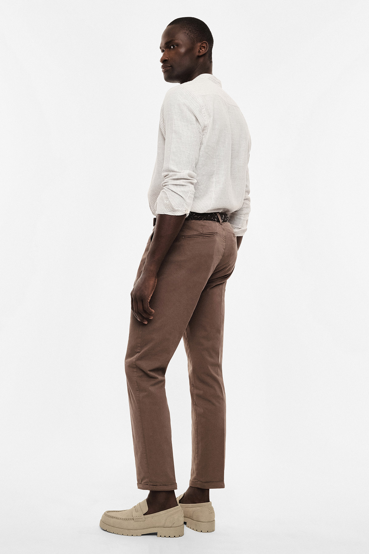 Man looking over shoulder in studio wearing a white shirt, brown chinos, braided belt and beige loafers — smart-casual outfit