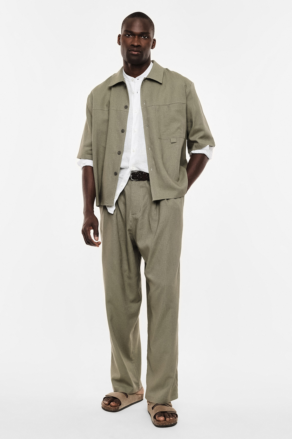 Male modelling relaxed olive two-piece suit with white shirt and brown sandals, full-length on white background