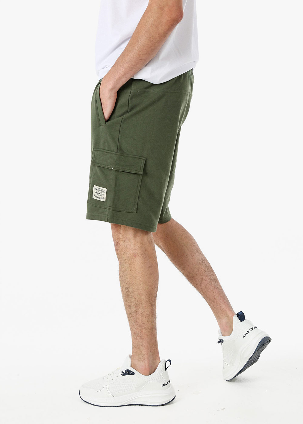 Male model wearing olive green cargo shorts with flap side pocket and white trainers, walking side view