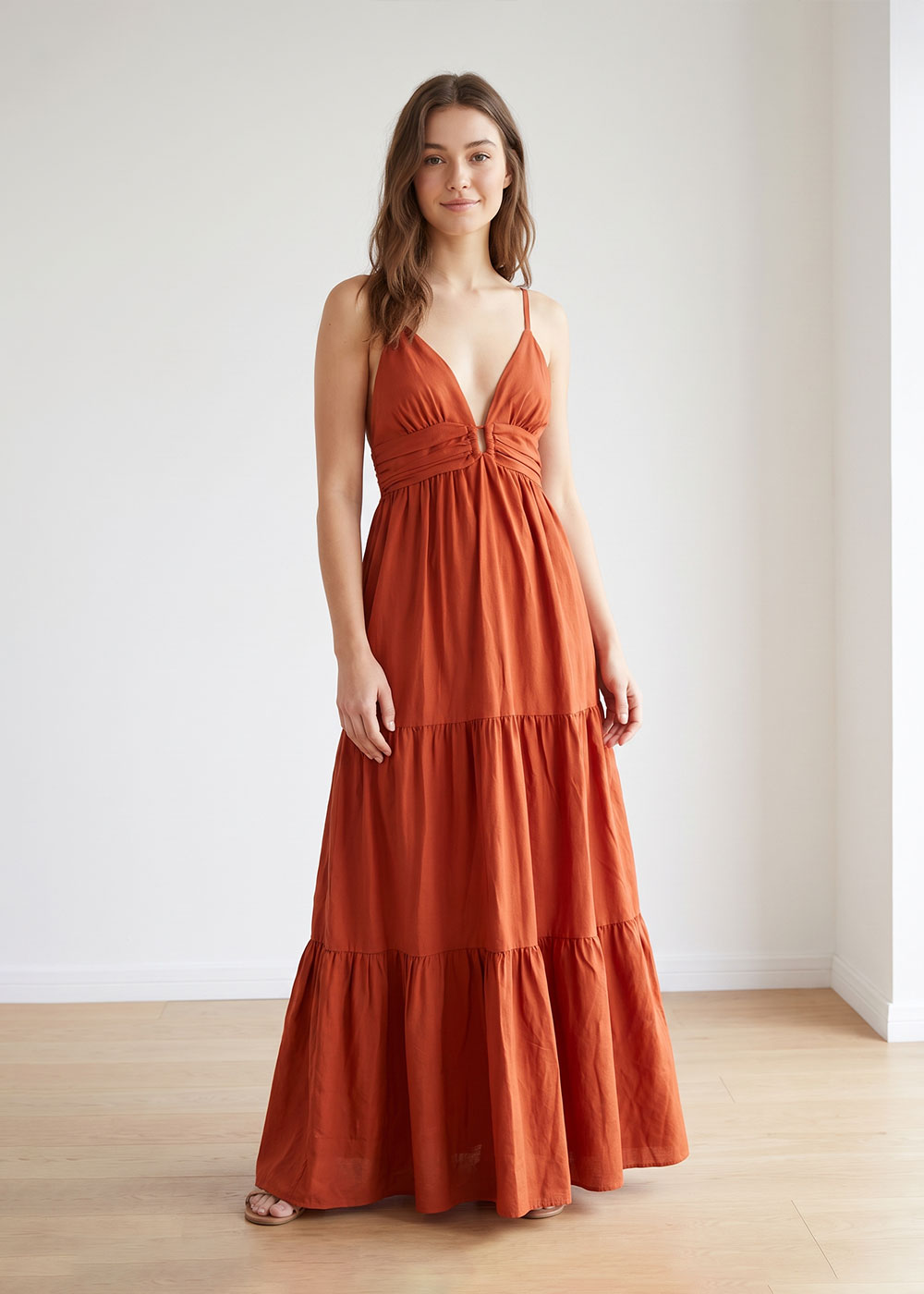 Woman modelling rust-coloured tiered maxi dress with spaghetti straps and V-neck in a minimal studio setting