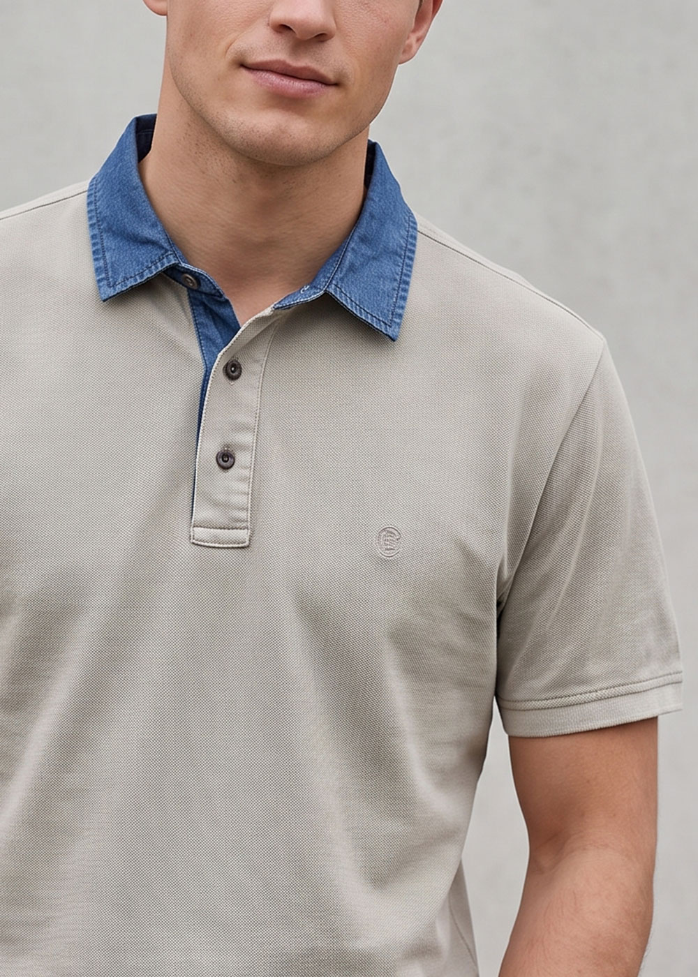 Close-up of a man wearing a beige polo shirt with a contrasting blue denim collar and three-button placket against a neutral background
