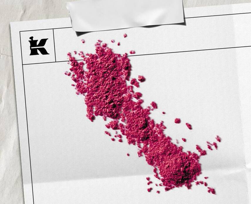 Polvere granulare fucsia sparsa in diagonale su un foglio bianco fisurato, con logo Kiehl's in alto a sinistra