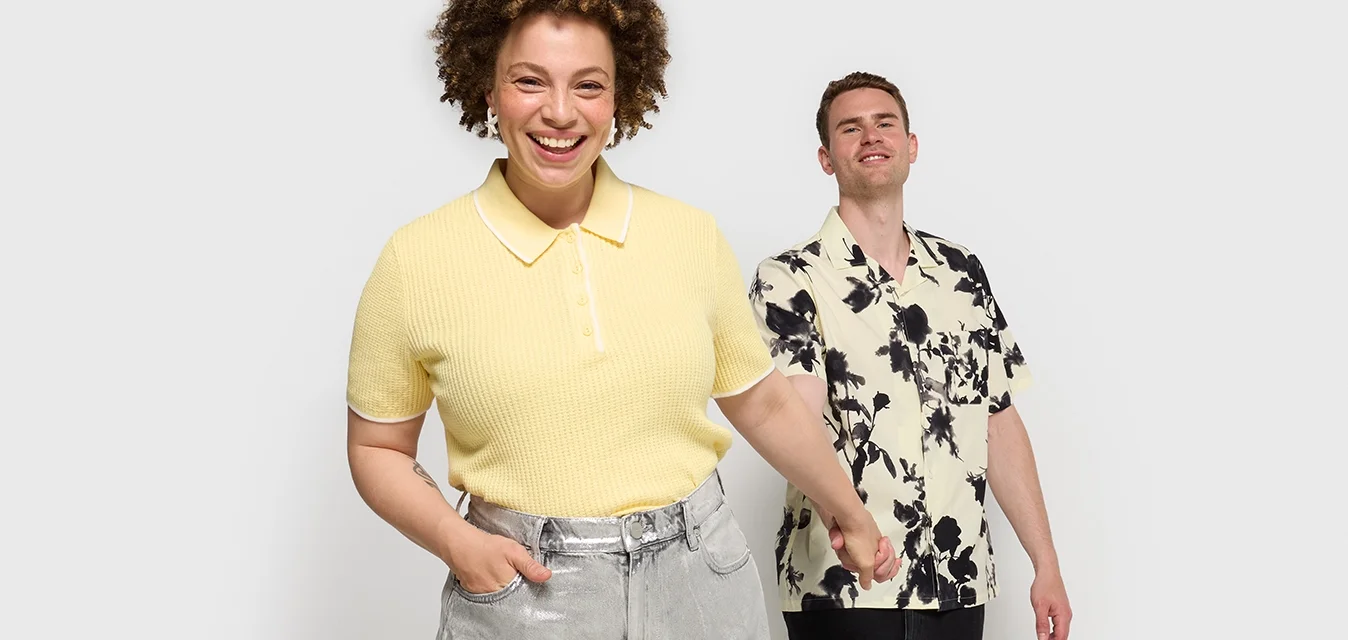 Polo shirt giallo a coste con colletto bianco, abbinato a pantaloni larghi argentati. Camicia a maniche corte leggera con motivi floreali in toni neri e beige.